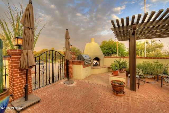 patio terrace at dusk featuring an outdoor fireplace and area for grilling