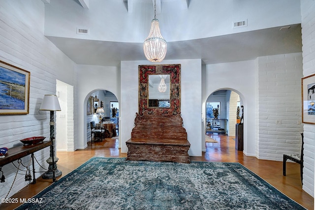 foyer entrance with a high ceiling, wood-type flooring, brick wall, and a notable chandelier