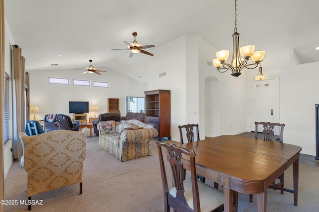 carpeted dining area with ceiling fan with notable chandelier and high vaulted ceiling