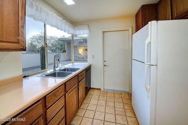 kitchen featuring a sink, freestanding refrigerator, brown cabinets, and dishwashing machine