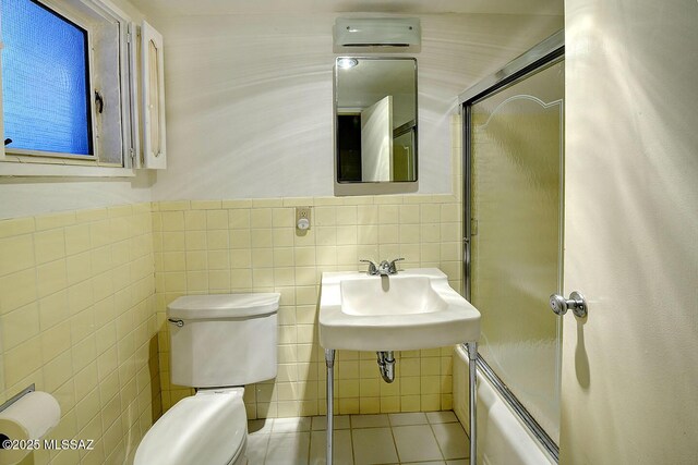 full bathroom with toilet, tile walls, tile patterned floors, a sink, and combined bath / shower with glass door