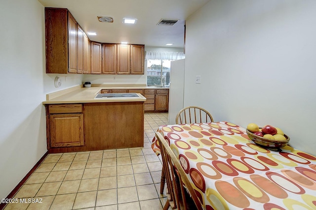 kitchen featuring freestanding refrigerator, a peninsula, light countertops, brown cabinets, and light tile patterned floors