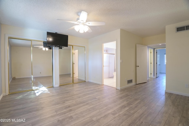 unfurnished bedroom with connected bathroom, two closets, ceiling fan, light hardwood / wood-style floors, and a textured ceiling