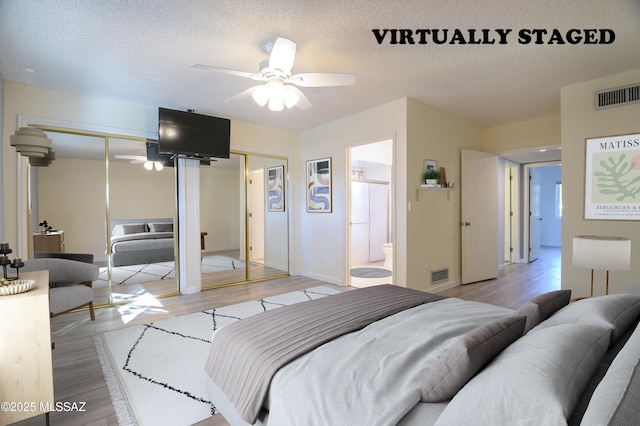 bedroom featuring ensuite bath, ceiling fan, light hardwood / wood-style floors, a textured ceiling, and multiple closets