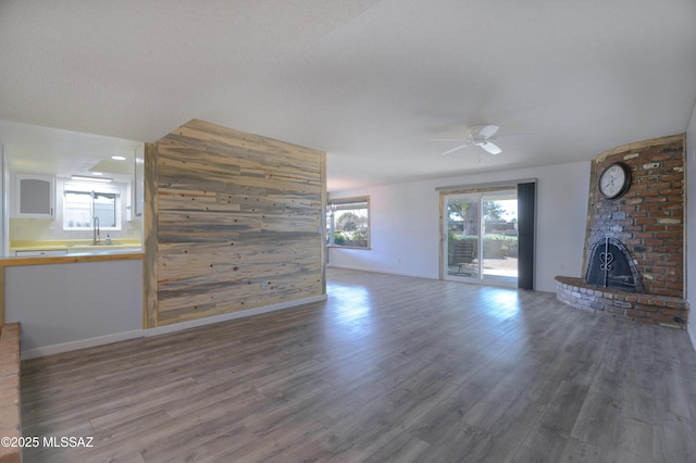 unfurnished living room with sink, ceiling fan, wooden walls, a fireplace, and dark hardwood / wood-style flooring