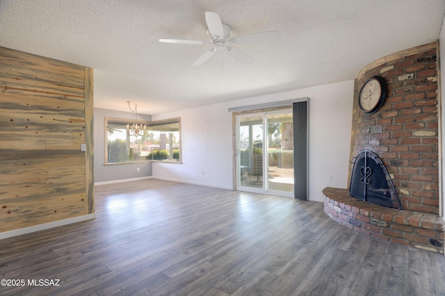 unfurnished living room with a fireplace, ceiling fan with notable chandelier, dark wood-type flooring, and a textured ceiling