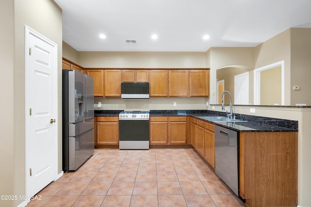 kitchen featuring stainless steel appliances, sink, light tile patterned floors, and dark stone counters