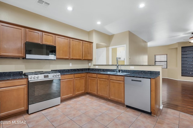 kitchen with appliances with stainless steel finishes, sink, dark stone counters, light tile patterned floors, and kitchen peninsula