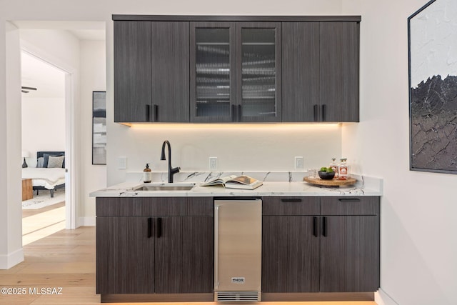 bar with light hardwood / wood-style floors, sink, dark brown cabinets, and light stone countertops