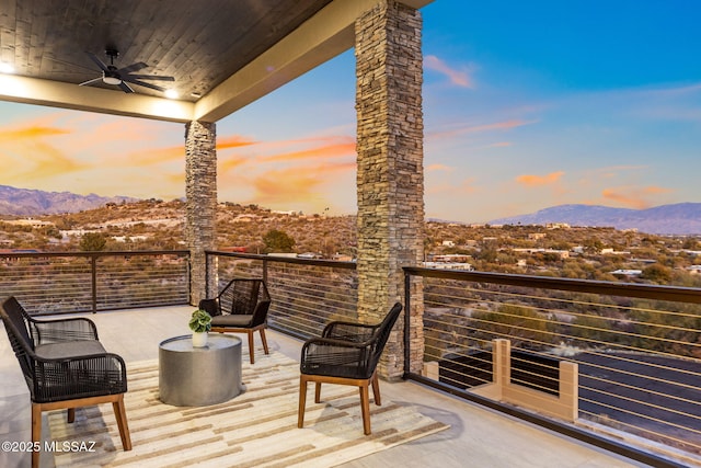 patio terrace at dusk with a mountain view, ceiling fan, and a balcony