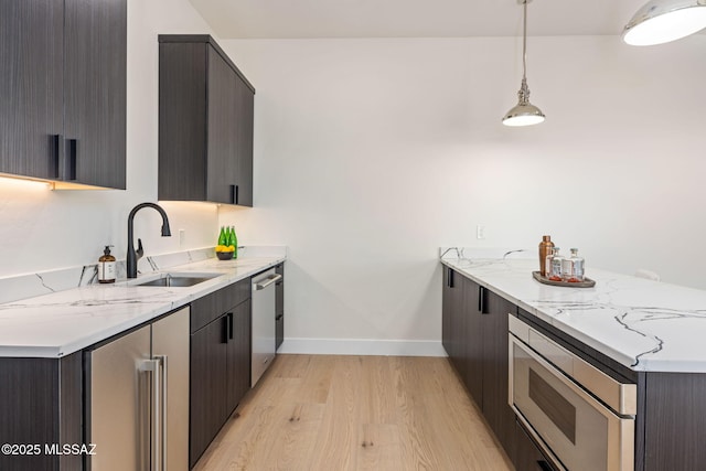 kitchen featuring light stone countertops, decorative light fixtures, stainless steel appliances, light hardwood / wood-style floors, and sink