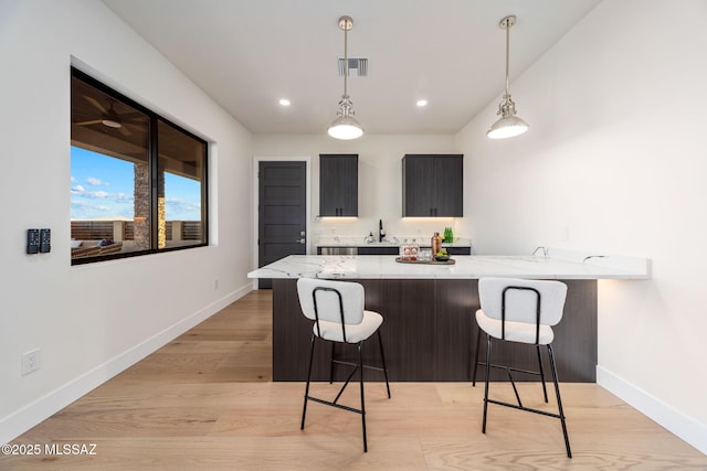 bar featuring decorative light fixtures, light stone countertops, sink, and light wood-type flooring