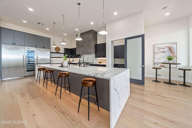 kitchen with a spacious island, hanging light fixtures, stainless steel built in refrigerator, light hardwood / wood-style floors, and decorative backsplash