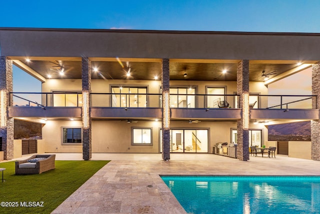 back house at dusk featuring a balcony, a patio area, and ceiling fan