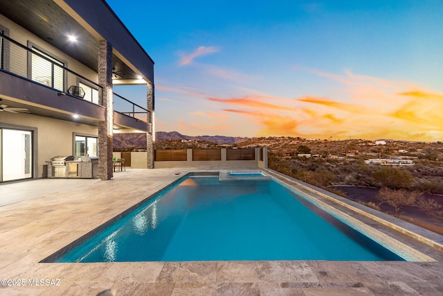 pool at dusk featuring exterior kitchen, a patio area, an in ground hot tub, and ceiling fan