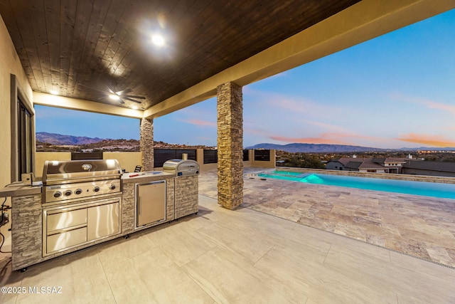 patio terrace at dusk featuring a mountain view, an outdoor kitchen, and grilling area