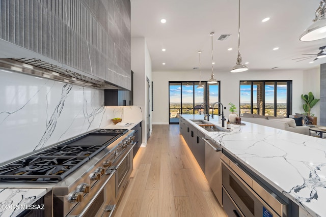 kitchen with light stone countertops, tasteful backsplash, custom range hood, hanging light fixtures, and sink