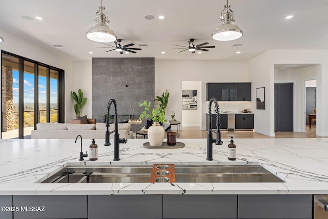 kitchen featuring sink, decorative light fixtures, light stone counters, and a tiled fireplace