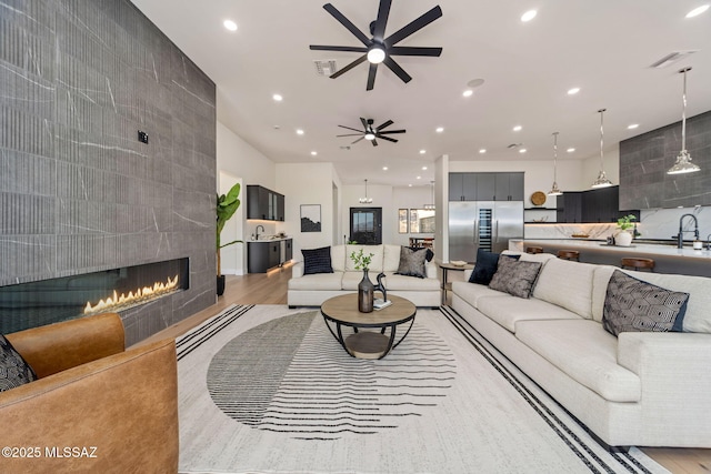 living room with light hardwood / wood-style floors, sink, a tile fireplace, and ceiling fan