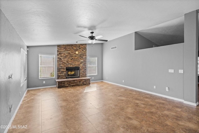 unfurnished living room featuring ceiling fan, a stone fireplace, a textured ceiling, and a healthy amount of sunlight