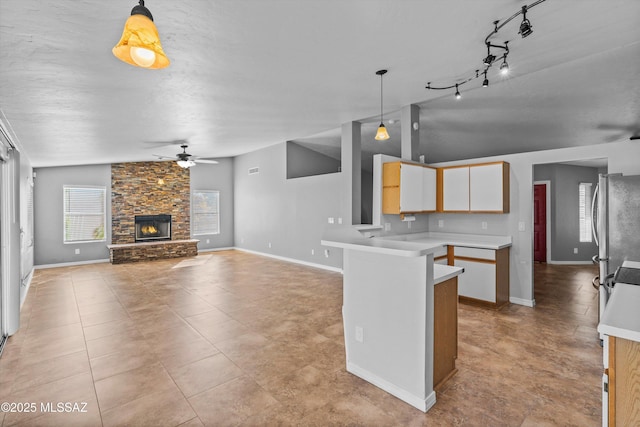 kitchen with a fireplace, stainless steel refrigerator, hanging light fixtures, ceiling fan, and kitchen peninsula