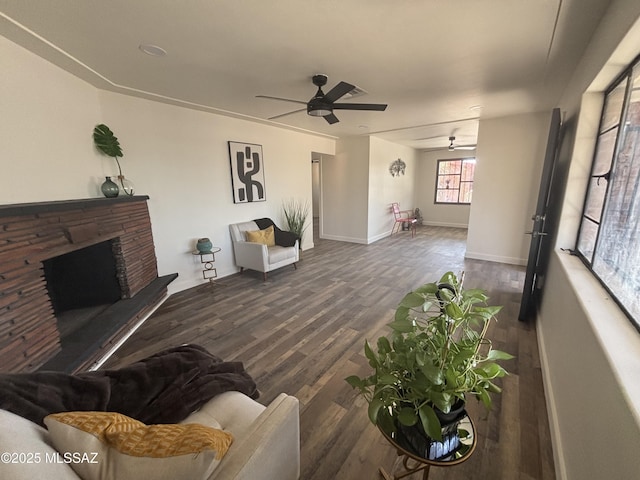 living room featuring dark wood-type flooring, ceiling fan, and a stone fireplace