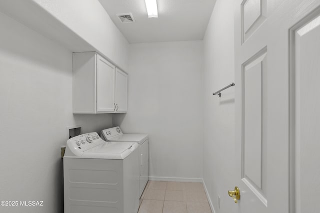 clothes washing area with cabinets, washing machine and dryer, and light tile patterned floors