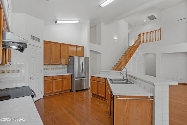 kitchen with sink, stainless steel fridge, hardwood / wood-style floors, a kitchen island with sink, and backsplash