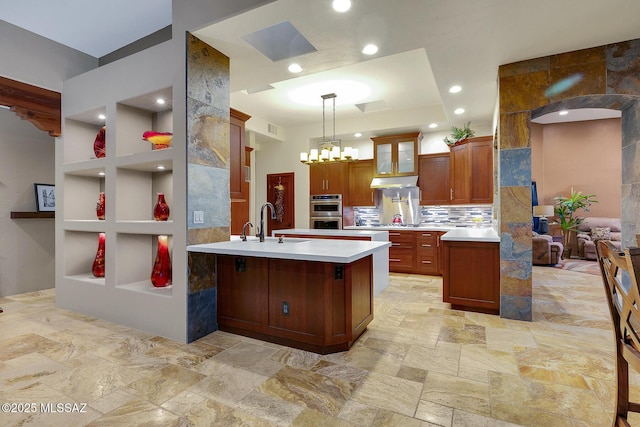 kitchen featuring sink, a center island with sink, pendant lighting, stainless steel double oven, and decorative backsplash