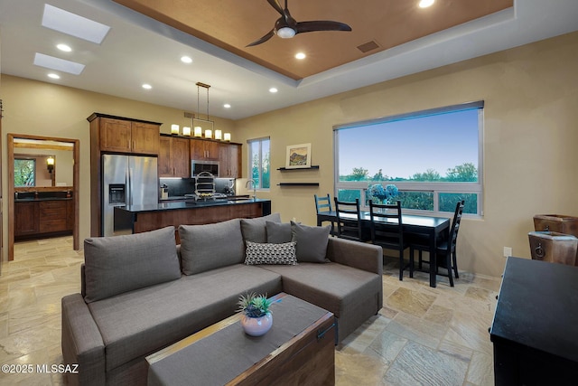 living room featuring sink, ceiling fan, and a tray ceiling