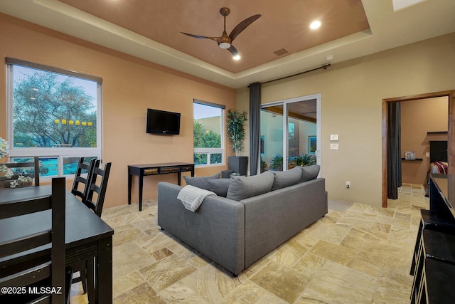 living room with a raised ceiling, a healthy amount of sunlight, and ceiling fan