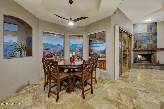 dining space featuring a raised ceiling, a mountain view, a large fireplace, and ceiling fan