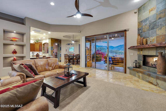 living room featuring a mountain view, a large fireplace, built in features, and ceiling fan