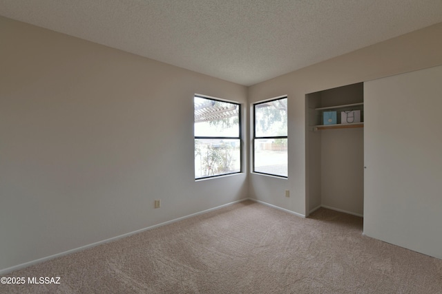 unfurnished bedroom featuring a textured ceiling, a closet, light colored carpet, and baseboards