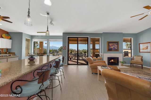 living room featuring light hardwood / wood-style floors, a tile fireplace, and ceiling fan