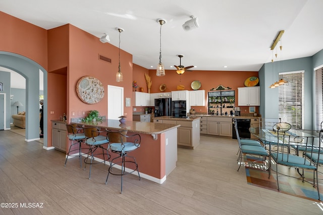 kitchen featuring sink, a kitchen breakfast bar, kitchen peninsula, light stone countertops, and black appliances