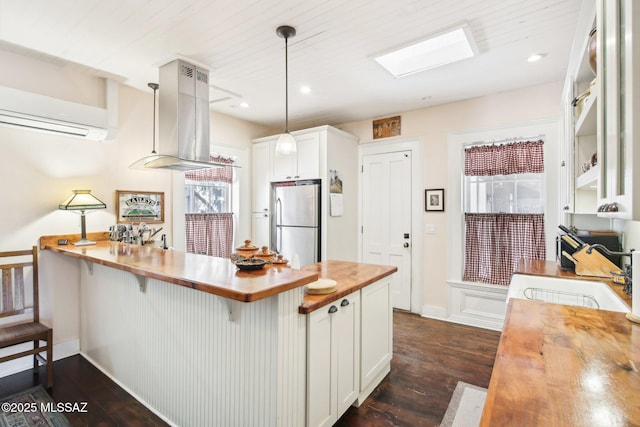 kitchen featuring white cabinetry, hanging light fixtures, island exhaust hood, a kitchen breakfast bar, and stainless steel fridge