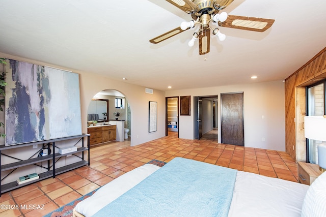 tiled bedroom with ceiling fan, wooden walls, and connected bathroom