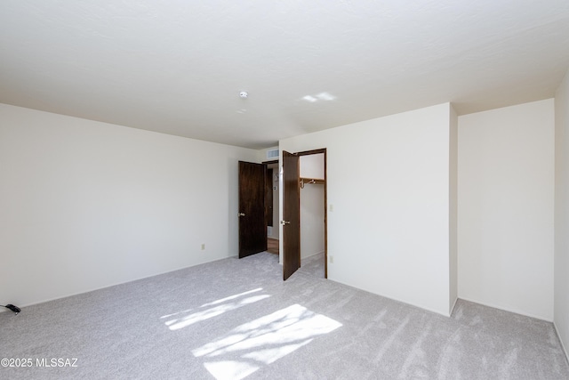 unfurnished bedroom featuring light carpet, a walk in closet, and a closet