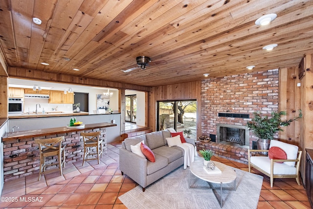 living room featuring a fireplace, light tile patterned flooring, sink, wooden walls, and wooden ceiling