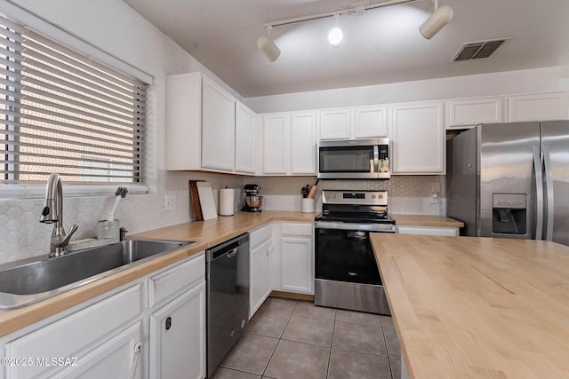 kitchen with white cabinets, wooden counters, stainless steel appliances, sink, and light tile patterned flooring