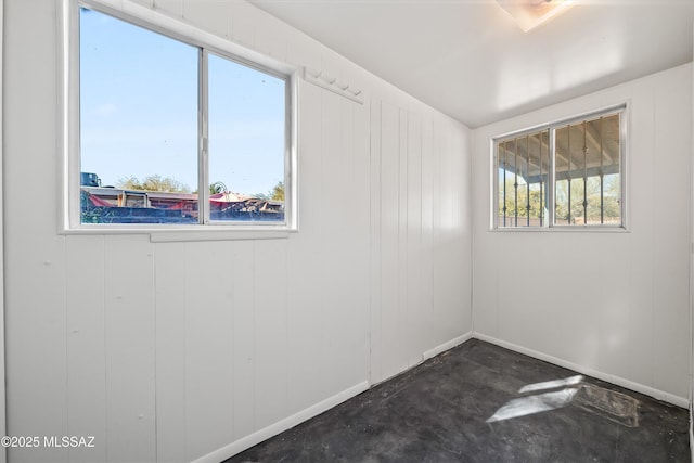 unfurnished room with baseboards, unfinished concrete flooring, and a healthy amount of sunlight