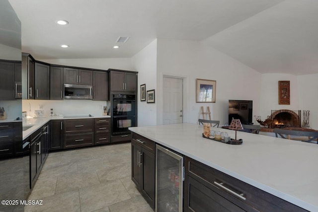 kitchen featuring black appliances, vaulted ceiling, beverage cooler, and dark brown cabinetry