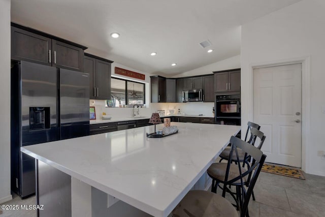 kitchen featuring light stone countertops, a kitchen island, a kitchen bar, stainless steel appliances, and vaulted ceiling