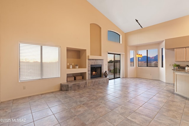 unfurnished living room with high vaulted ceiling, light tile patterned floors, and a tile fireplace