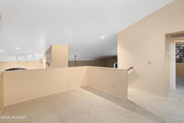 unfurnished room featuring rail lighting, lofted ceiling, and light carpet