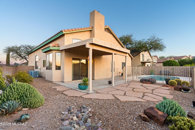 back house at dusk with a fenced in pool, central air condition unit, and a patio area