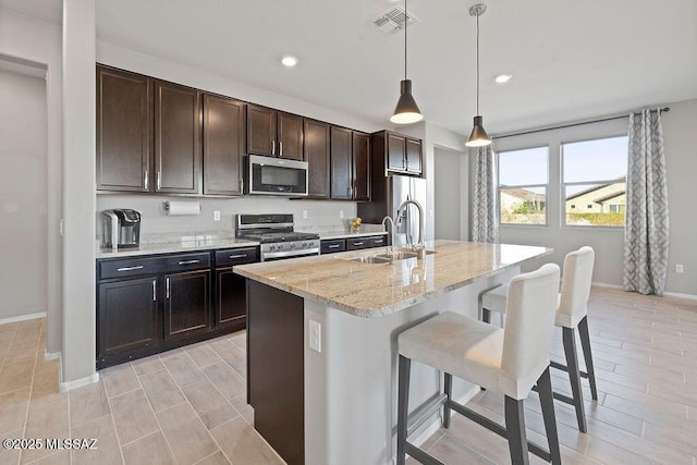 kitchen with sink, appliances with stainless steel finishes, a kitchen island with sink, hanging light fixtures, and a kitchen breakfast bar