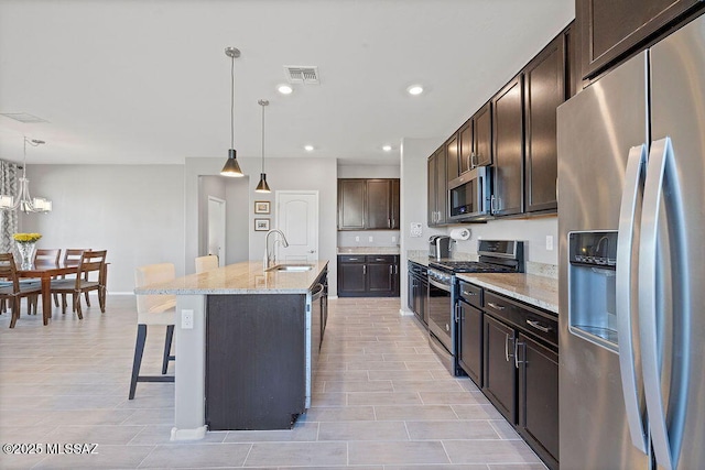 kitchen featuring a breakfast bar, sink, decorative light fixtures, appliances with stainless steel finishes, and a kitchen island with sink