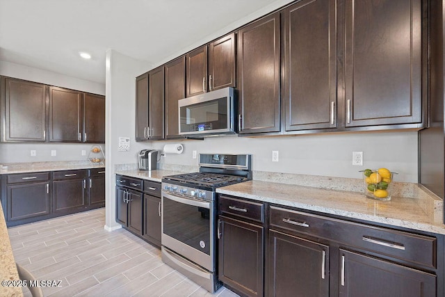 kitchen featuring dark brown cabinetry, light stone counters, and stainless steel appliances